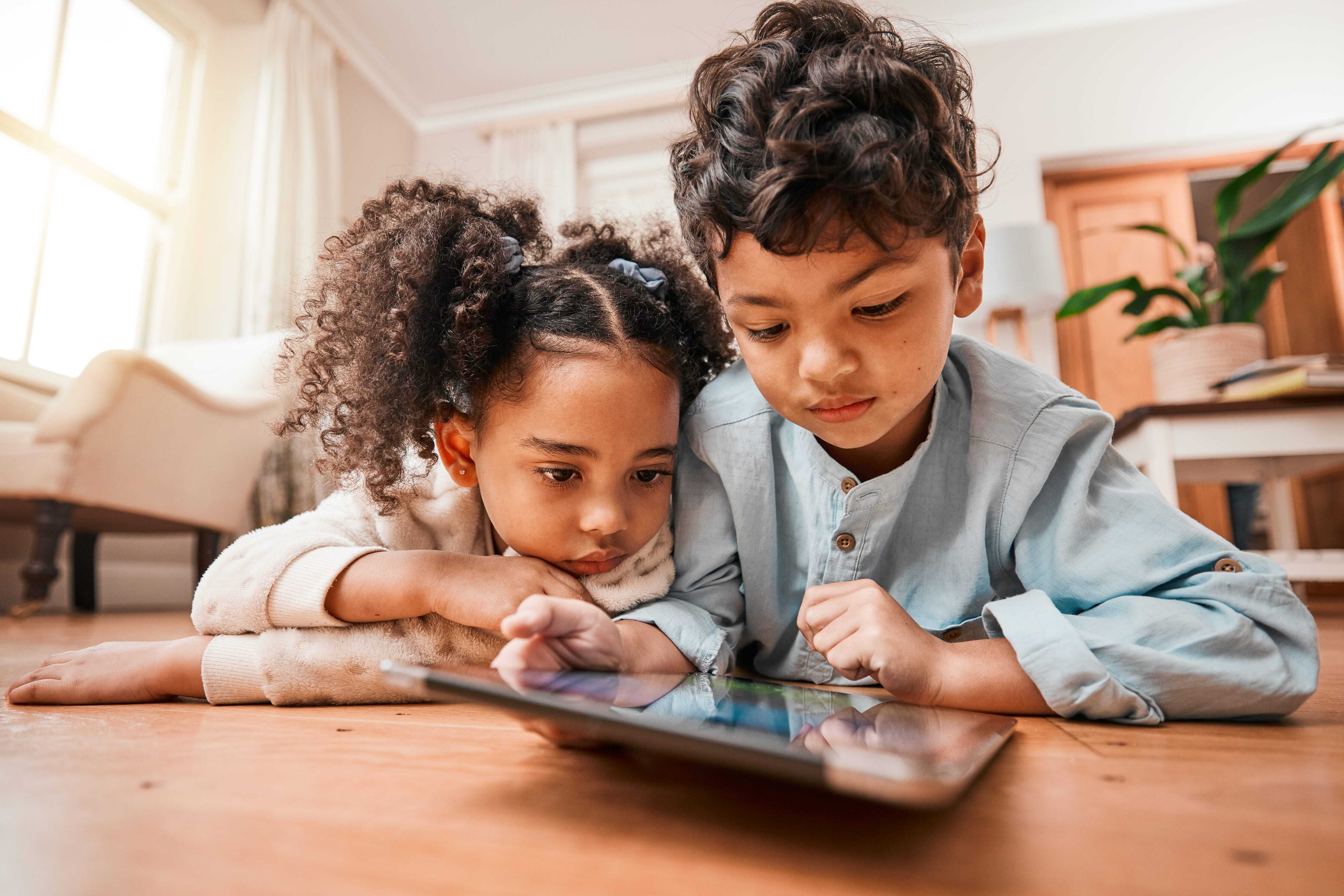 Two young children laying on the floor watching a tablet and enjoying some screen time together. 